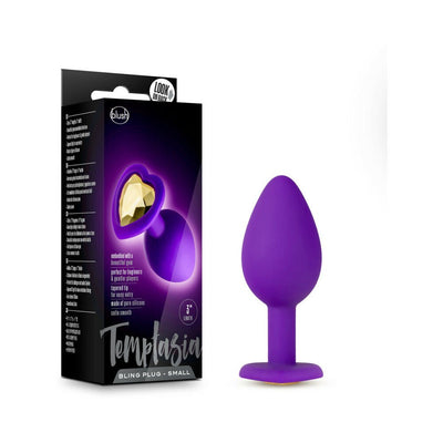 Small purple silicone anal plug with gold gem base next to black and purple Temptasia Bling Plug packaging.