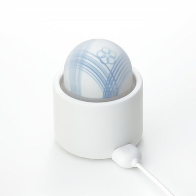 Tenga Iroha Temari Mizu in white and blue with floral design, shown in a white charging dock with USB cable attached.