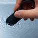 Hand holding a black silicone vibrating ring partially submerged in water, demonstrating its waterproof feature.