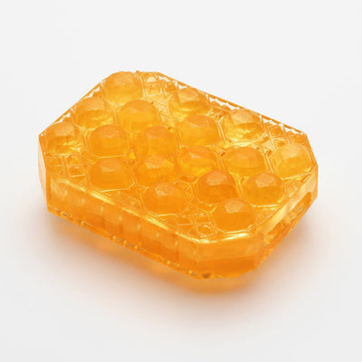 Transparent amber textured Tenga Uni pleasure sleeve with raised geometric pattern on a white background.