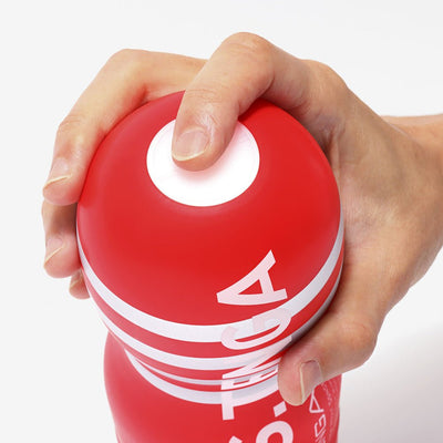Hand holding and pressing the top of a red Tenga U.S. Original Vacuum Cup Strong device with white branding.
