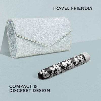 Black vibrator with white floral pattern next to a sparkly silver clutch purse, highlighting travel-friendly compact design.
