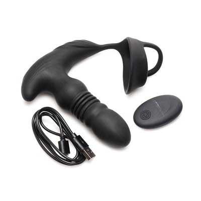 Black silicone thrusting vibrator with attached cock and ball ring, wireless remote control, and USB charging cable on white background.