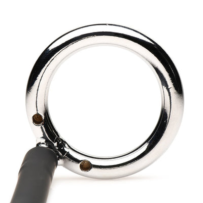 Close-up of a shiny metal cock and ball ring attached to a black silicone cord on a white background.