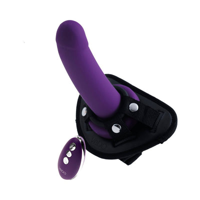 Deep purple rechargeable vibrating strap-on with adjustable black harness and matching remote control.