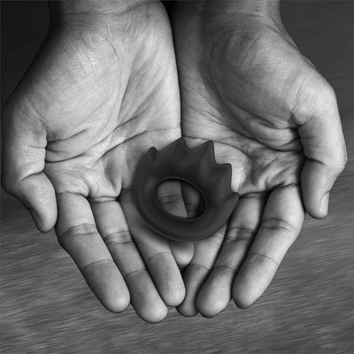 Hands holding a black silicone cock ring with five mountain peak-like projections in a soft oval shape.