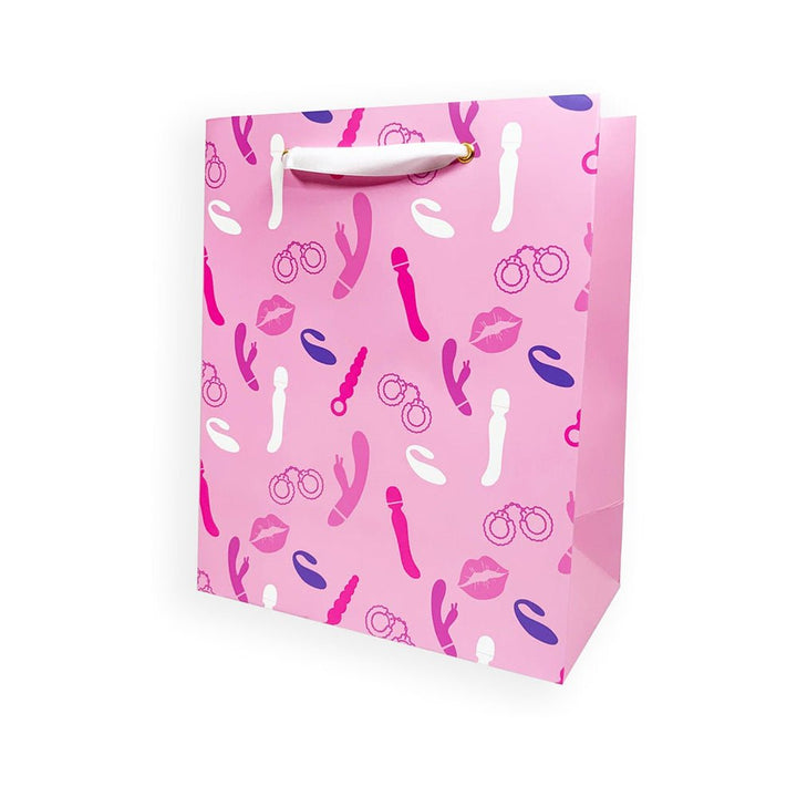 Pink gift bag with playful vibrator and handcuff illustrations, white ribbon handles, and gold grommets.