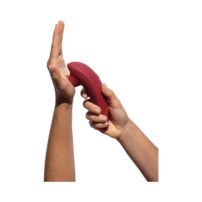 Hands holding a Womanizer Premium 2 clitoral stimulator in raspberry color against a white background.