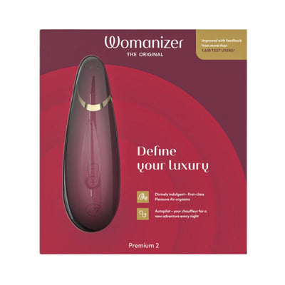 Womanizer Premium 2 clitoral stimulator in burgundy with gold accents on red packaging box.
