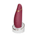 Womanizer Premium 2 clitoral stimulator in burgundy with gold accent on a white charging stand