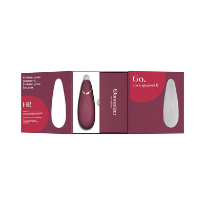 Womanizer Premium 2 clitoral stimulator in burgundy with gold accents displayed in open luxury packaging.