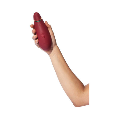 Hand holding a Bordeaux Womanizer Premium 2 clitoral stimulator with control buttons visible on the front.