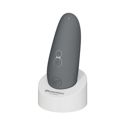 Gray Womanizer Starlet 3 clitoral stimulator with control buttons on white charging stand.