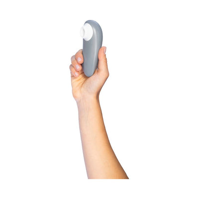 Hand holding a gray Womanizer Starlet 3 clitoral stimulator with white silicone head on a white background.