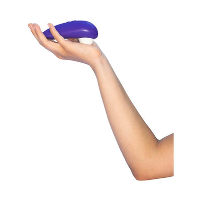 Hand holding a purple Womanizer Starlet 3 clitoral stimulator with a white silicone head against a white background.