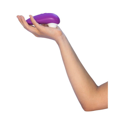 Hand holding a purple Womanizer Starlet 3 clitoral stimulator with white silicone head against a white background.