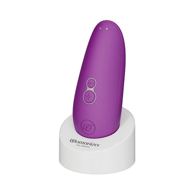 Purple Womanizer Starlet 3 clitoral stimulator standing on white charging base with control buttons visible
