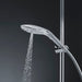 Sleek chrome Womanizer Wave shower head with water flowing, mounted on adjustable shower rail against dark background.