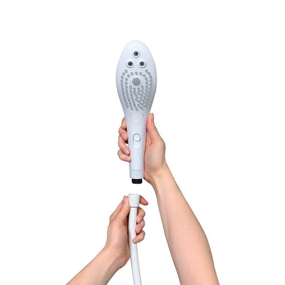 Hands holding a white Womanizer Wave shower head and hose, showing connection point on a white background.