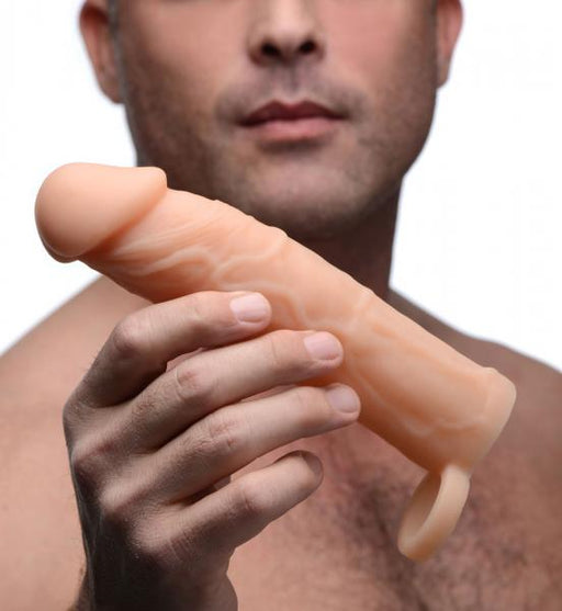 Man holding a beige silicone penis extension with textured veins and a ring for secure fit.