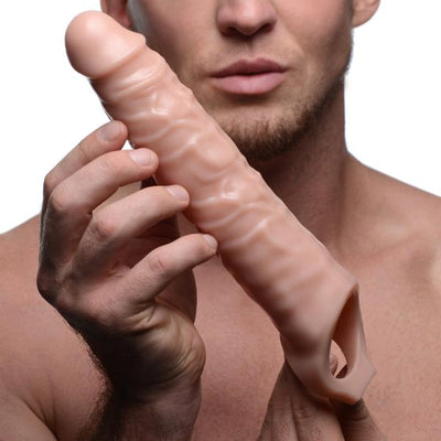 Man holding a beige 3-inch realistic textured penis extender sleeve with hollow interior and ball strap opening.