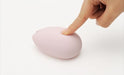 Hand pressing the smooth, pink Tenga Iroha Sakura massager with a soft-touch finish on a white surface.