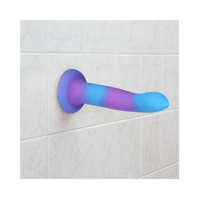 Purple and blue glow-in-the-dark silicone dong with suction base attached to white tiled wall