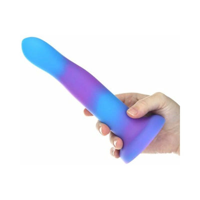 Hand holding a bendable purple and blue glow-in-the-dark silicone dong with a strong suction base.