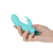 Hand holding a compact turquoise silicone vibrator with a removable rabbit-shaped sleeve and metallic base.