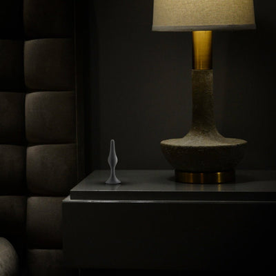 Medium black silicone beginner plug standing upright on a dark bedside table next to a textured lamp.