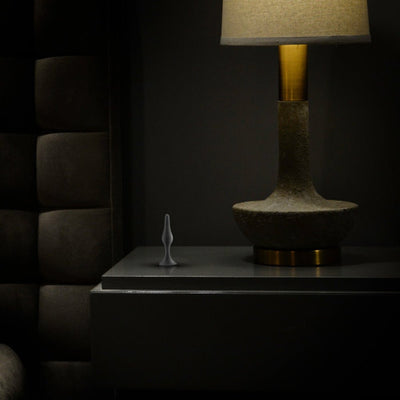 Small black silicone beginner plug displayed on a bedside table next to a modern lamp in a dimly lit room.