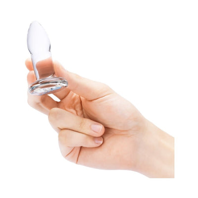 Hand holding a small clear glass anal dilator with a smooth tapered shape and flared base.