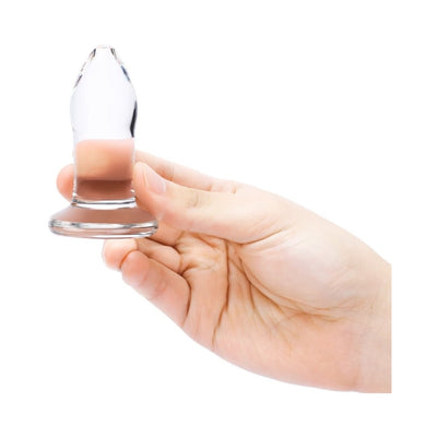 Hand holding a clear glass anal dilator with a smooth, tapered design and flared base on a white background.