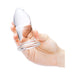 Hand holding a clear, smooth glass anal dilator with a rounded tip and flared base.