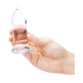 Hand holding a clear, smooth glass anal dilator with a tapered tip and flared base against a white background.