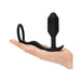 Hand holding a black weighted silicone anal plug with an attached flexible penis ring.