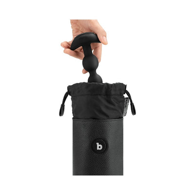 Hand placing a black silicone toy into a black B-Vibe UV Sterilizer Pouch with drawstring closure and textured exterior.