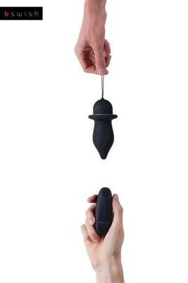 Hand holding black B Swish Bfilled Classic Unleashed plug with pull-string and wireless remote control against white background.
