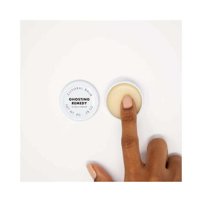 Open jar of Bijoux Indiscrets Clitherapy Ghosting Remedy clitoral balm with finger touching the smooth balm surface on a white background.