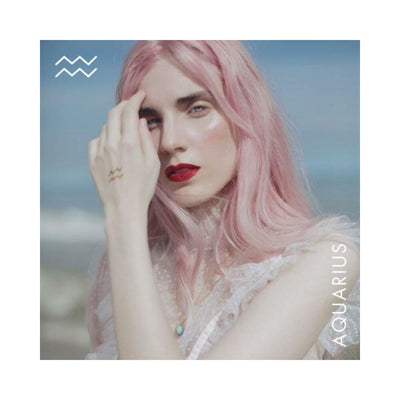 Woman with pink hair wearing a turquoise necklace and showing Aquarius zodiac symbol on her hand against a soft blue background.