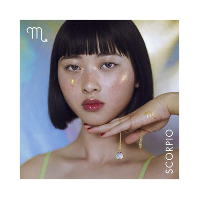 Close-up of a woman with a Scorpio tattoo on her hand, holding a gold chain necklace with an opal pendant against a soft colorful background.