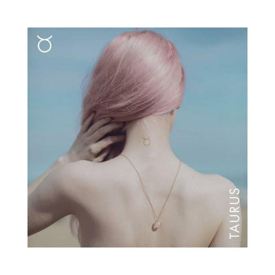 Woman with pink hair showing a rose quartz necklace and Taurus zodiac symbol tattoo on her upper back against a blue sky background.