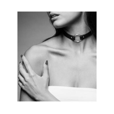 Black vegan leather choker with a silver ring detail worn on the neck, styled with bare shoulders and a white top.