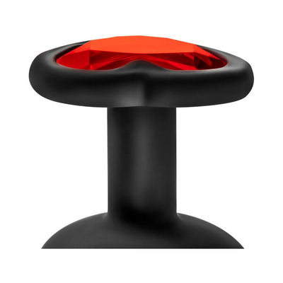 Close-up of black silicone plug base with red heart-shaped gem inset, smooth finish and tapered neck design.
