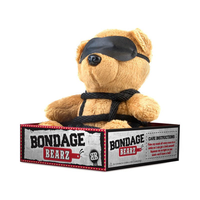 Plush teddy bear wearing a black eye mask and faux leather harness, seated in a Bondage Bearz branded box.