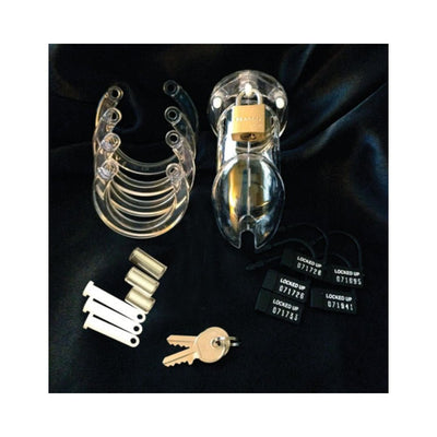 Clear male chastity device with multiple sized rings, locking pins, brass padlock with keys, and numbered plastic locks on black fabric background.