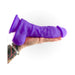 Hand holding a thick 8-inch purple silicone dildo with suction cup base against a white background.