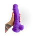 Hand holding a thick 8-inch purple silicone realistic dildo with suction base against a white background.
