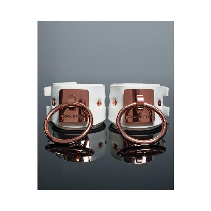 White vegan leather cuffs with rose gold metal rings and engraved Coquette plates, adjustable buckle closures.