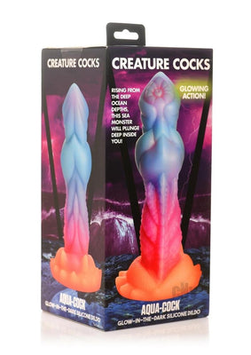 Packaging of Creature Cocks Aqua Cock glow-in-the-dark silicone dildo with blue and pink gradient design and suction cup base.